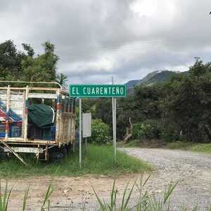 Sign for "El Guariento" next to a parked trailer and a dirt road in a rural area.