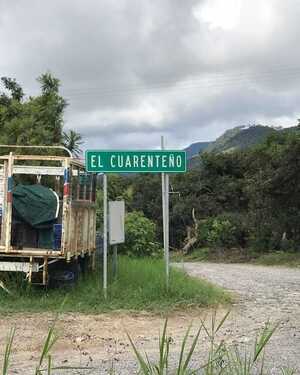 Sign for "El Guariento" next to a parked trailer and a dirt road in a rural area.